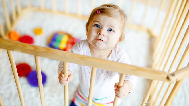 toddler holding barrier of playpen